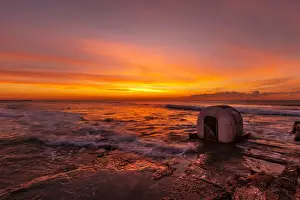 Beautiful red, yellow and orange colors of a sunrise over the ocean with a little concrete hut