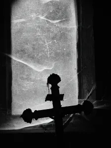 Halloween Prints: Close-up of a crucifix photographed against the light in front of a window covered by dust