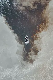 Drone photo looking down on a speedboat between clouds of sediment flowing down the Mary River, Northern Territory, Australia