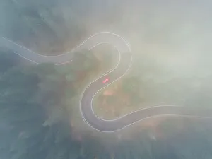 Drone shot through low cloud above a winding forest road, Dolomites, Italy Drone shot through low cloud above a winding forest road, Dolomites, Italy