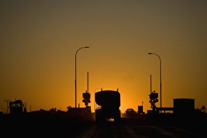 A freight truck and car stopped at a railroad crossing silhouetted against the setting sun A freight truck and car stopped at a railroad crossing silhouetted against the setting sun