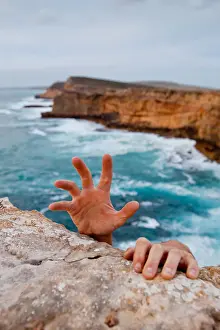 Hands reaching up to grip a cliff. Dangerous ocean in the background