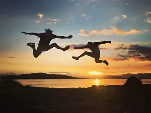 Vitality Prints: Silhouette of two men jumping into the sunset sky