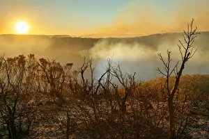 Sun setting in burnt smouldering mountain landscape with smoke filled valley after forest