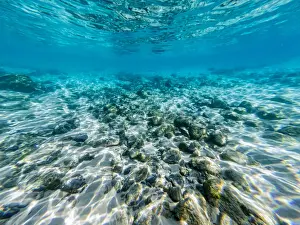 Underneath a wave in the clear ocean waters looking at rocks and shells on the ocean floor